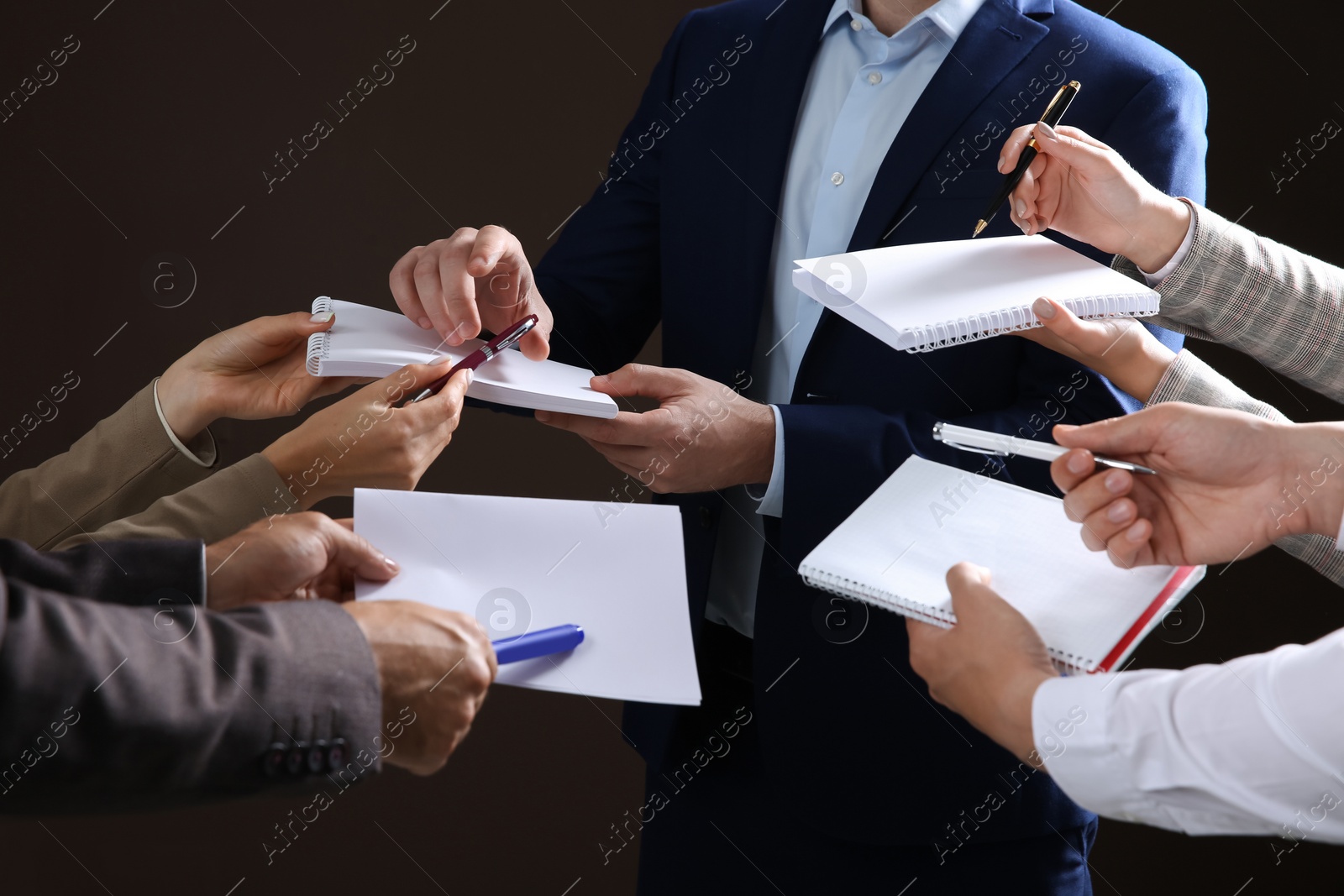 Photo of Man signing autograph in notebooks on dark background, closeup