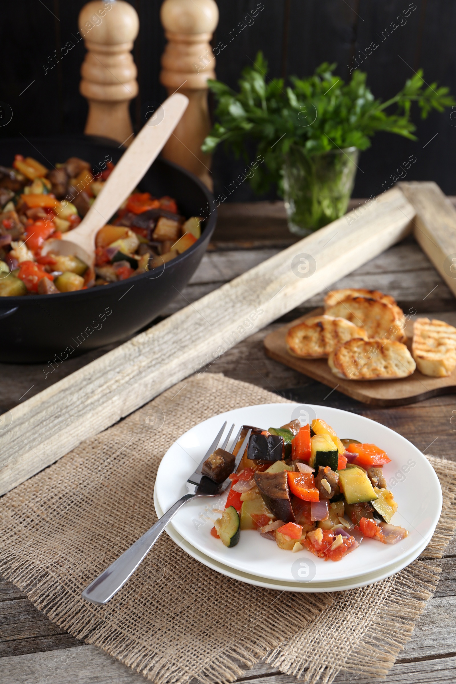 Photo of Delicious ratatouille served with bread on wooden table