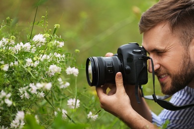 Photo of Male photographer taking picture of beautiful plants with professional camera outdoors