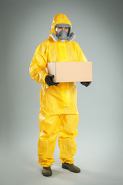 Photo of Man wearing chemical protective suit with cardboard box on light grey background. Prevention of virus spread