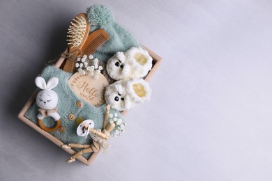 Photo of Wooden box with baby clothes, booties and accessories on grey background, top view. Space for text