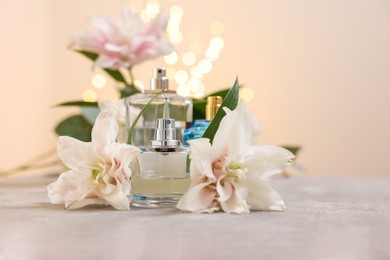 Bottles of perfume and beautiful lily flowers on table against beige background with blurred lights, closeup. Space for text