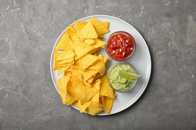 Plate with delicious mexican nachos chips and sauces on grey table, top view