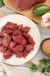 Photo of Pieces of raw beef meat, spices and products on light wooden table, flat lay