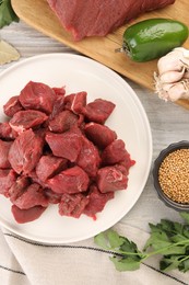 Pieces of raw beef meat, spices and products on light wooden table, flat lay