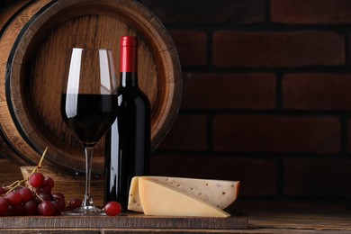 Delicious wine, cheese, grapes and wooden barrel on table against brick wall. Space for text