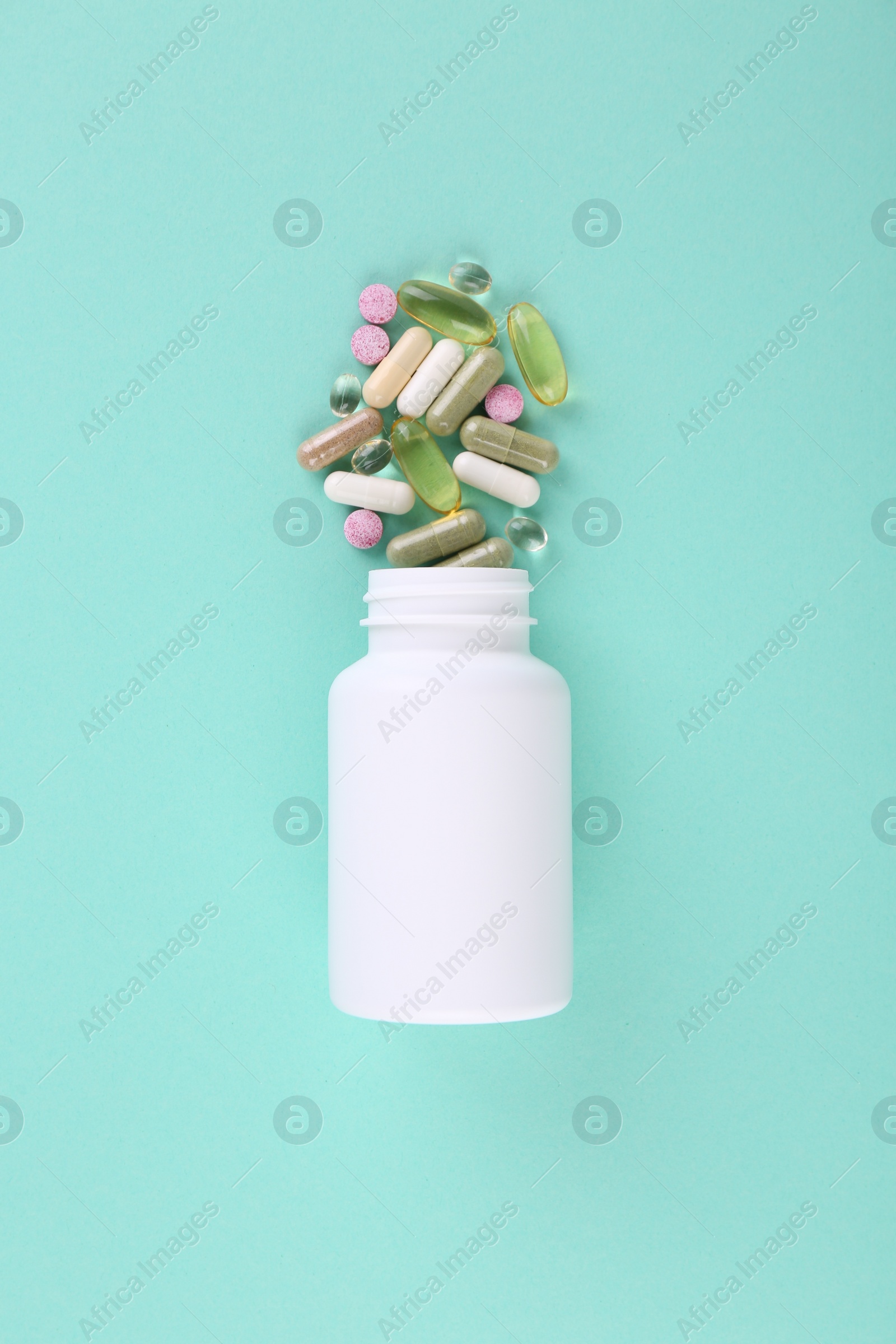 Photo of Bottle and different vitamin pills on turquoise background, top view