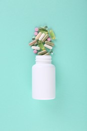 Bottle and different vitamin pills on turquoise background, top view