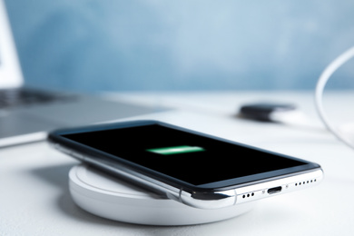 Photo of Mobile phone charging with wireless pad on white stone table, closeup. Space for text
