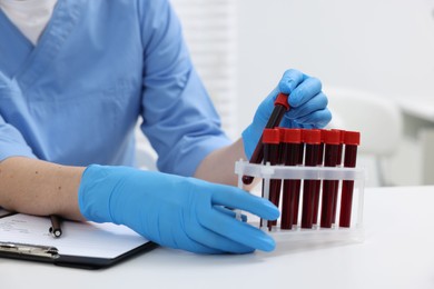 Laboratory testing. Doctor with blood samples in tubes at white table indoors, closeup