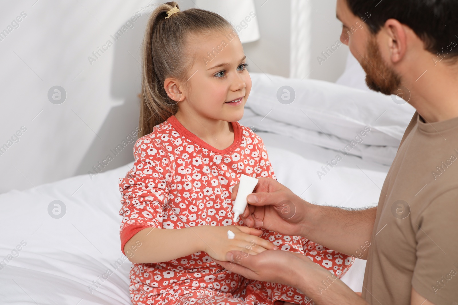 Photo of Father applying ointment onto her daughter's hand on bed