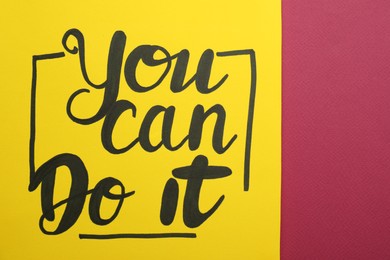 Photo of Yellow card with motivational phrase You Can Do It on burgundy background, closeup
