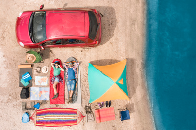 Couple with camping equipment near car on sand, aerial view. Summer trip