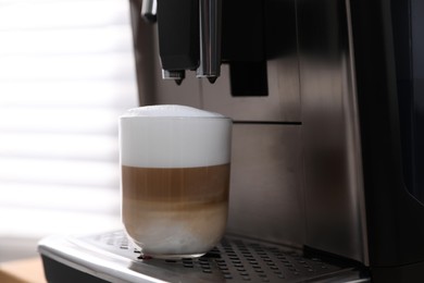 Photo of Modern coffee machine with cup of latte indoors, closeup