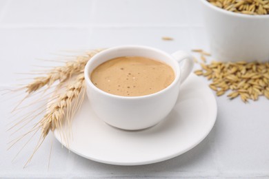 Cup of barley coffee, spikes and grains on white table, closeup