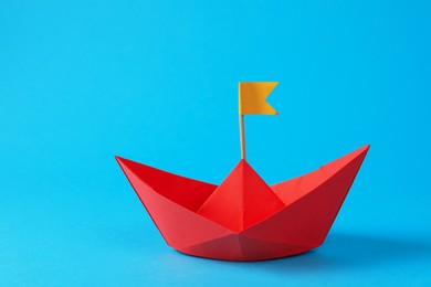 Photo of Handmade red paper boat with flag on light blue background