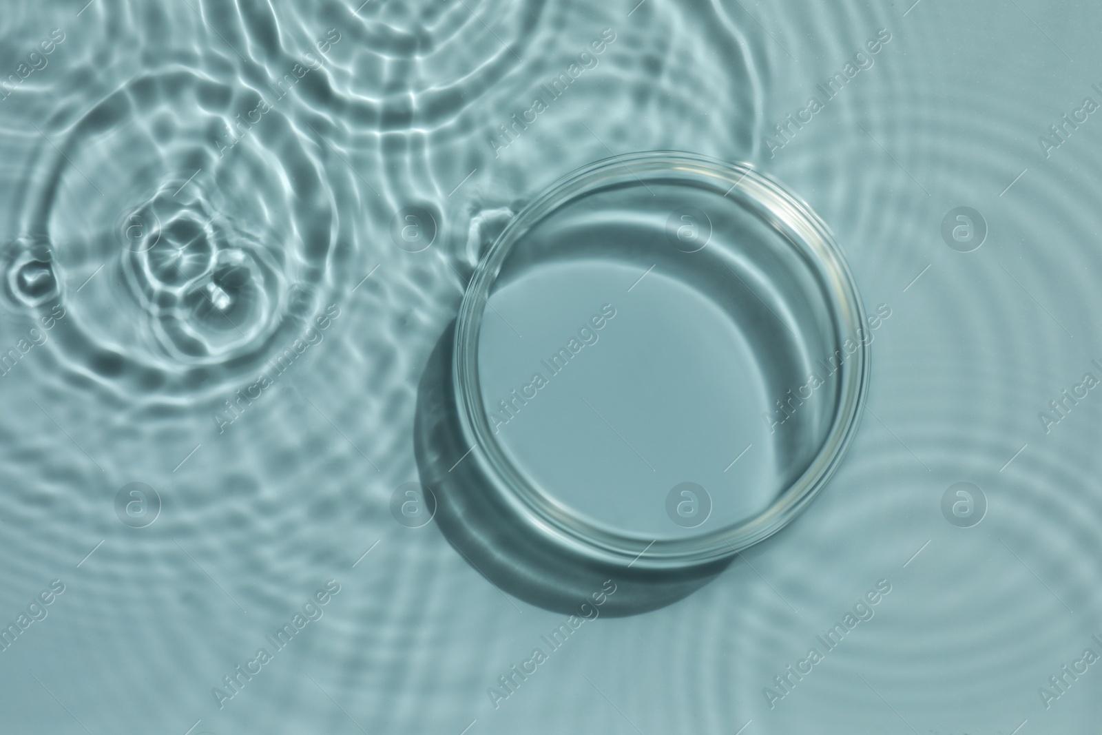 Photo of Stylish presentation for product. Glass podium in water on light blue background, top view