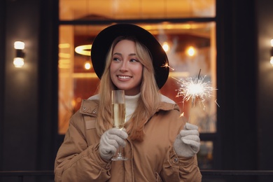 Photo of Happy young woman with sparkler and glass of champagne at winter fair