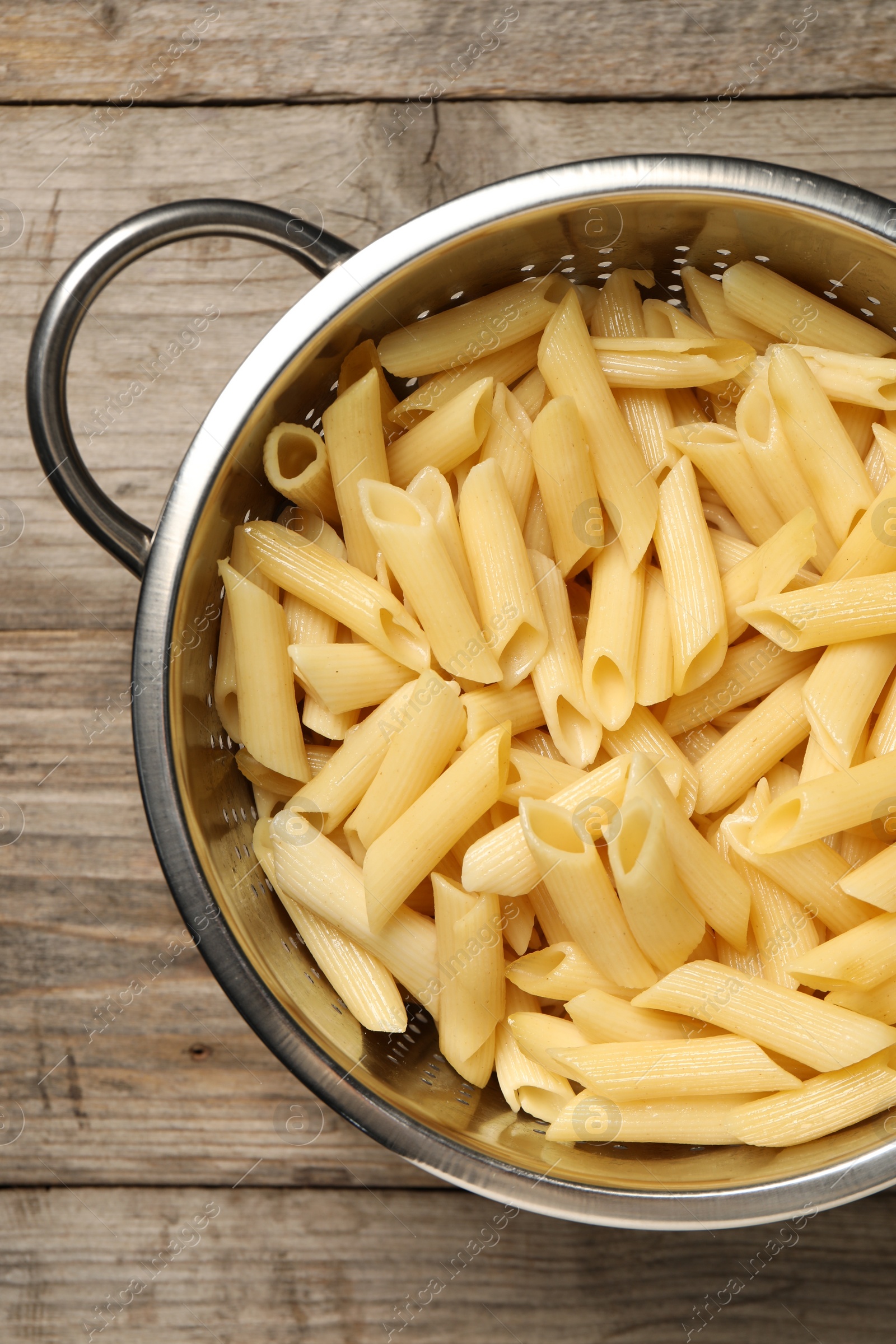 Photo of Delicious penne pasta in colander on wooden table, top view