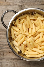 Photo of Delicious penne pasta in colander on wooden table, top view