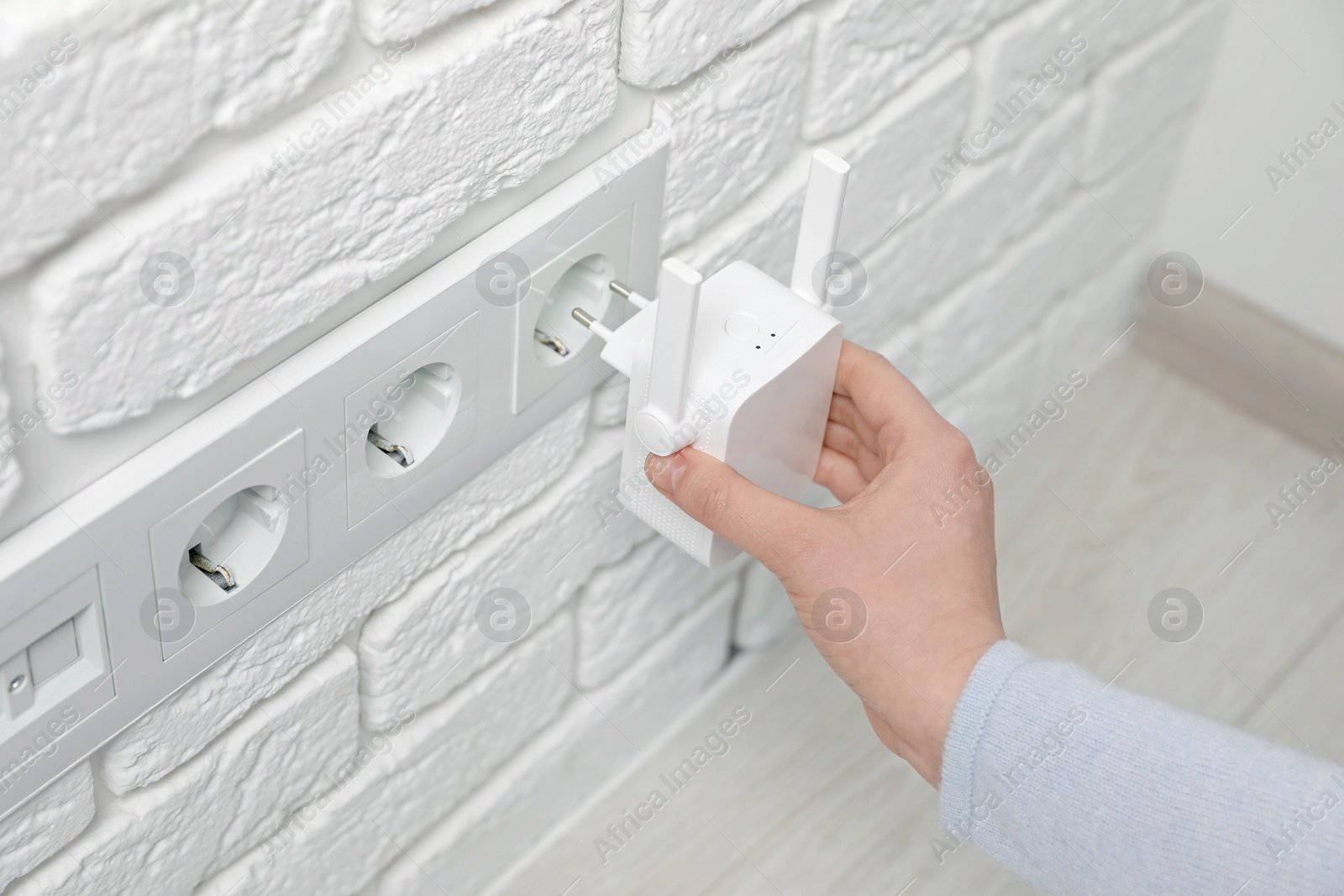 Photo of Woman inserting wireless Wi-Fi repeater into power socket indoors, closeup