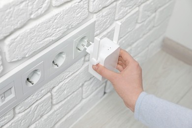 Woman inserting wireless Wi-Fi repeater into power socket indoors, closeup