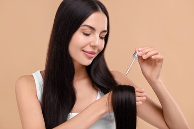 Photo of Beautiful woman applying hair serum on beige background. Cosmetic product