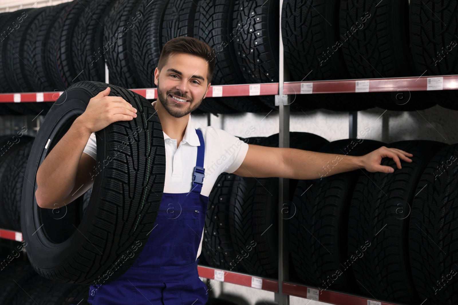 Photo of Male mechanic with car tire in auto store