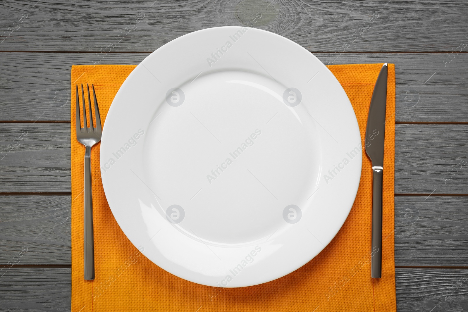 Photo of Clean plate and shiny silver cutlery on grey wooden table, flat lay