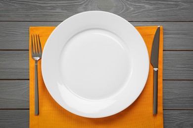Photo of Clean plate and shiny silver cutlery on grey wooden table, flat lay