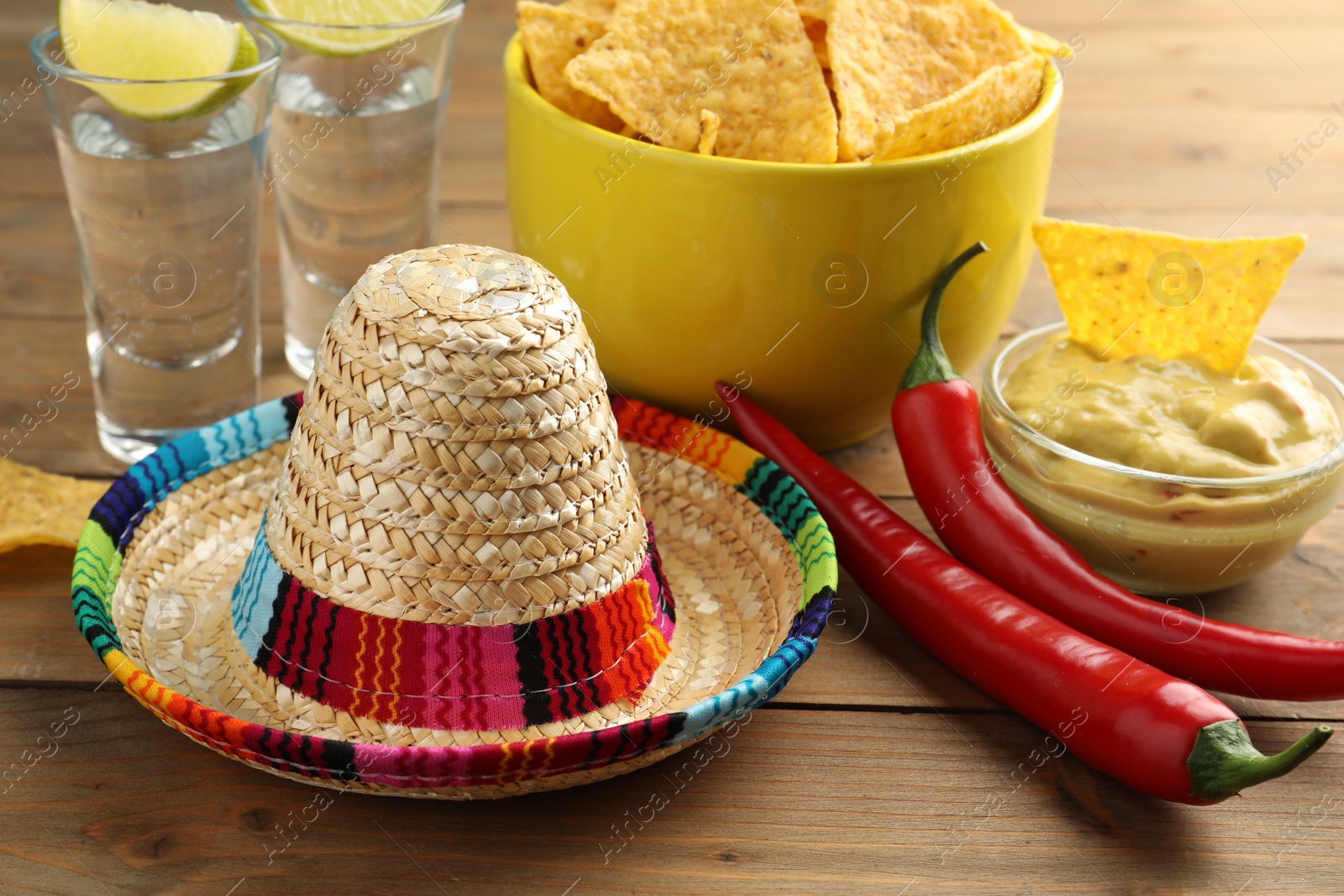 Photo of Mexican sombrero hat, tequila, chili peppers, nachos chips and guacamole on wooden table