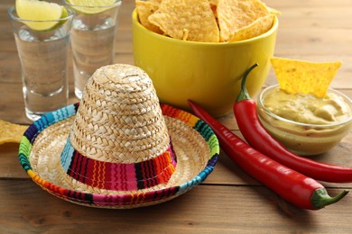 Mexican sombrero hat, tequila, chili peppers, nachos chips and guacamole on wooden table