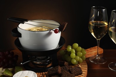 Photo of Forks with pieces of grape, bread, fondue pot with melted cheese, wine and snacks on table, closeup