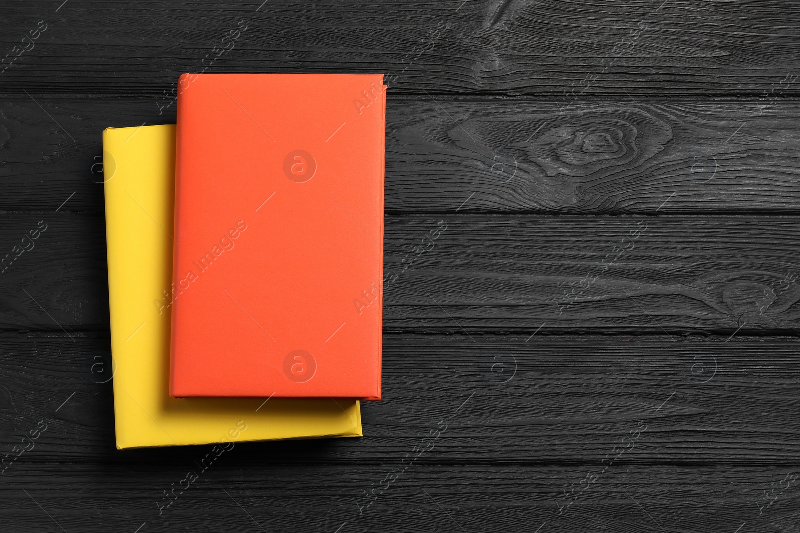 Photo of Orange and yellow books on black wooden table, top view. Space for text