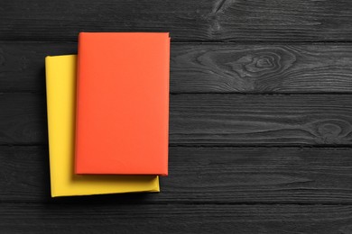 Photo of Orange and yellow books on black wooden table, top view. Space for text