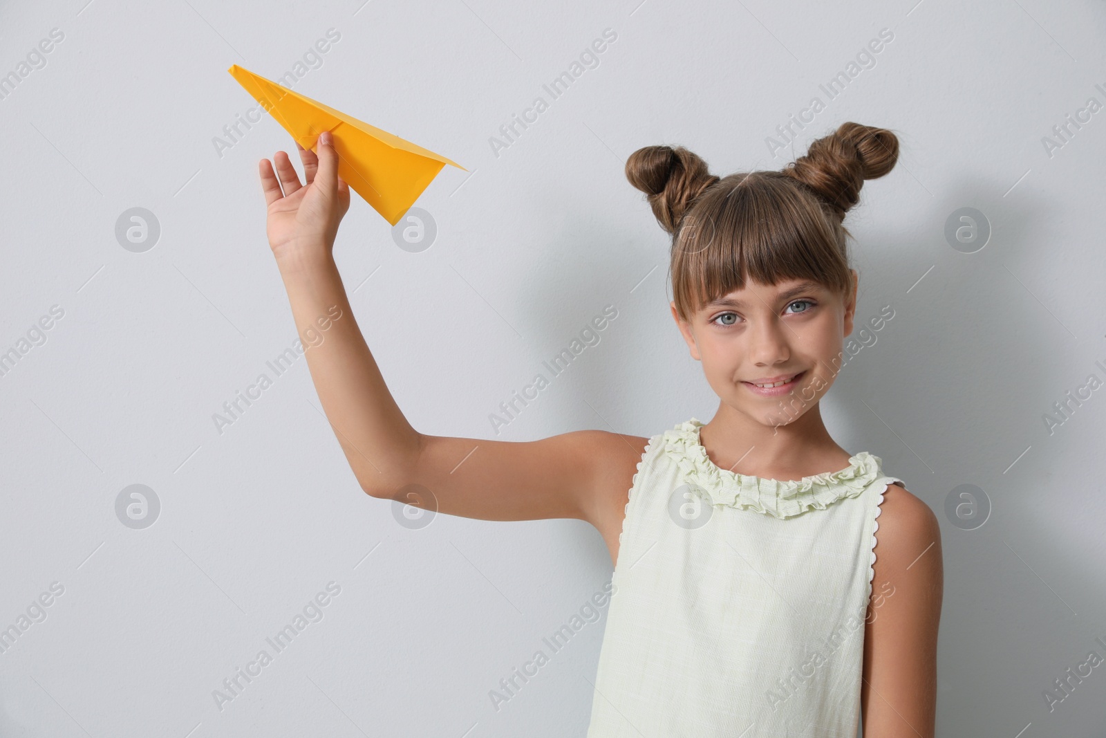 Photo of Cute little girl playing with paper plane on light grey background