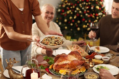 Photo of Woman with bowl of traditional Christmas kutia and her family at festive dinner, focus on hands. Slavic dish