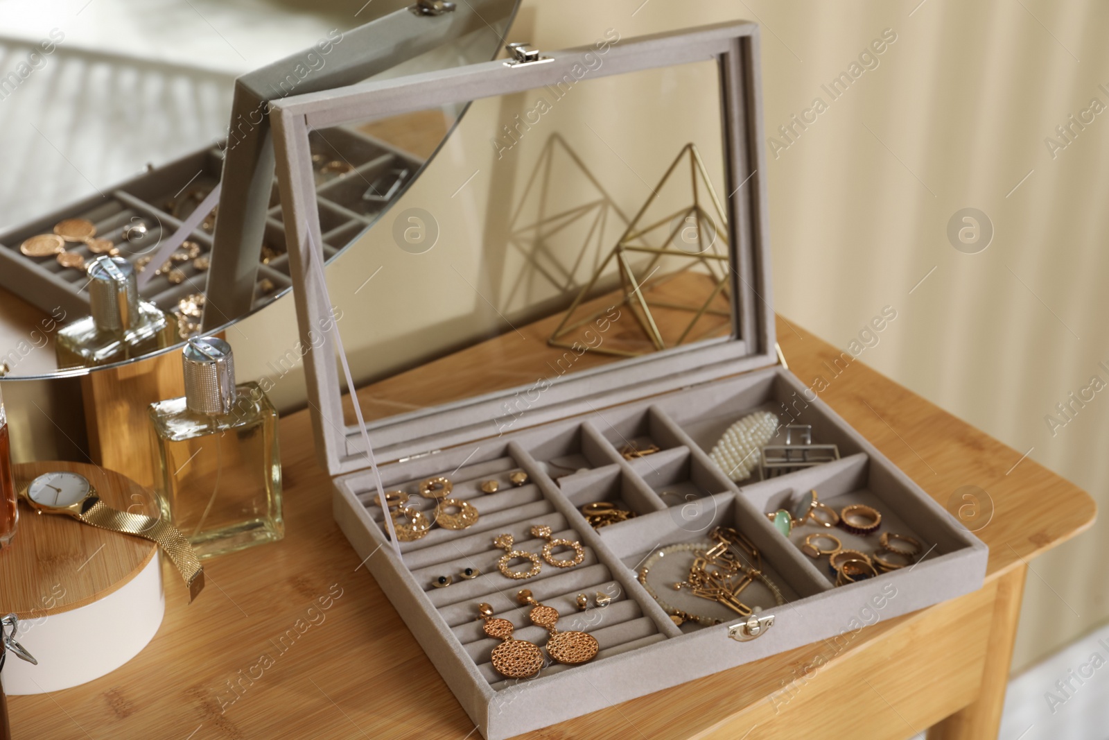 Photo of Elegant jewelry box with beautiful bijouterie, luxury perfume and stylish accessories on wooden table in room