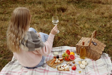 Photo of Young woman with glass of wine having picnic outdoors on autumn day, back view