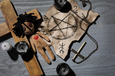 Photo of Female voodoo doll with heart and ceremonial items on grey wooden table, flat lay