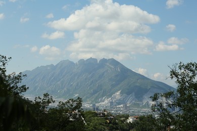 Photo of Picturesque view of mountains, city and trees under cloudy sky