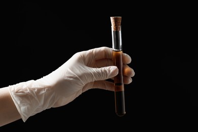 Photo of Scientist holding test tube with liquid on black background, closeup