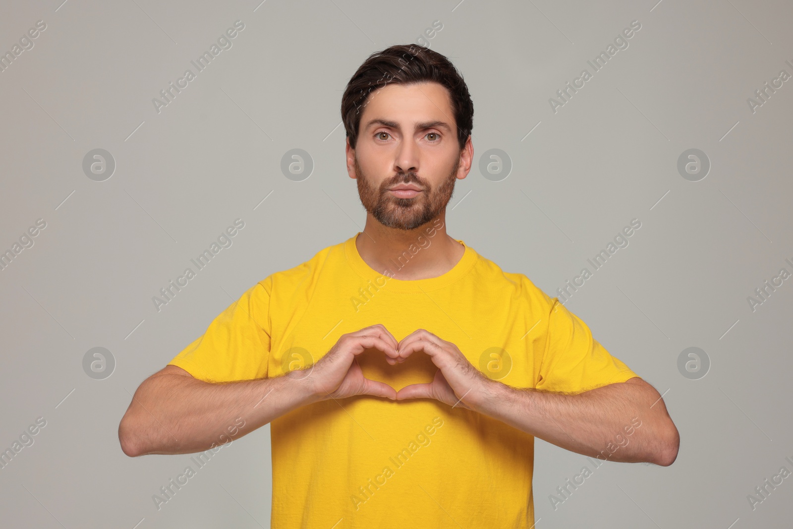 Photo of Handsome man making heart with hands and blowing kiss on light grey background
