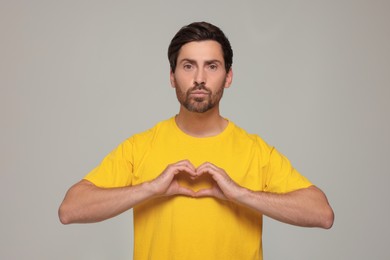 Handsome man making heart with hands and blowing kiss on light grey background
