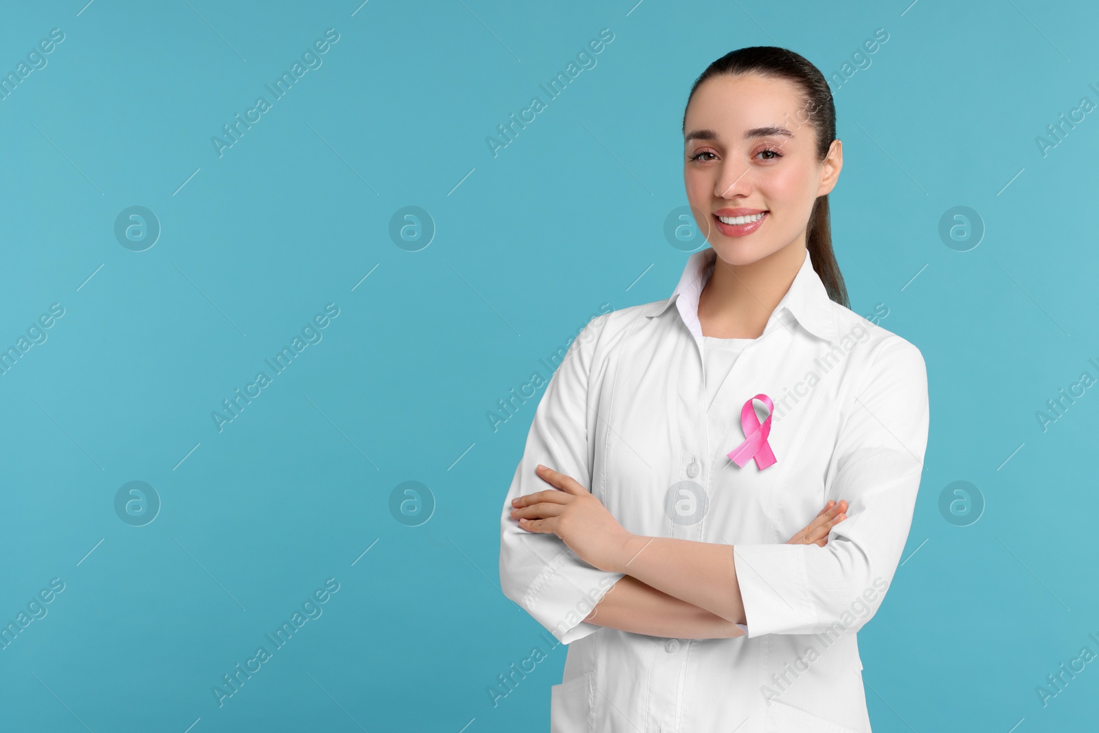 Photo of Mammologist with pink ribbon on light blue background, space for text. Breast cancer awareness