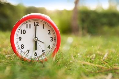 Photo of Red alarm clock on green grass outdoors. Space for text
