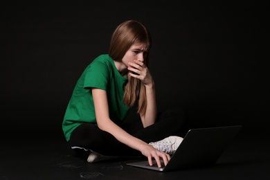 Photo of Terrified teenage girl with laptop on black background. Danger of internet