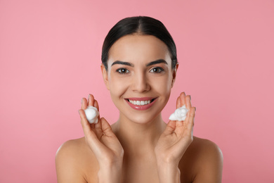 Photo of Young woman applying cosmetic product on pink background. Washing routine