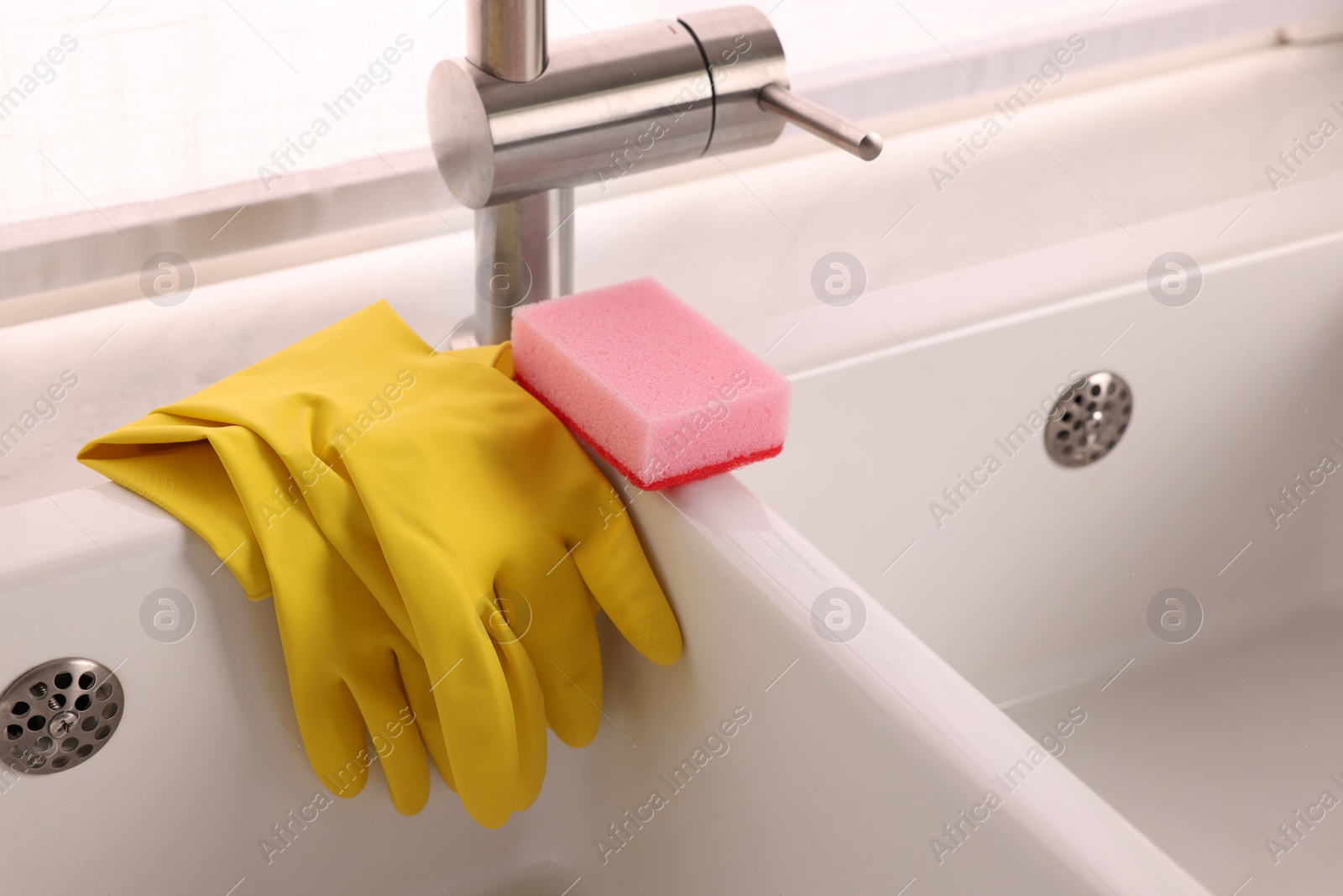 Photo of Sponge and rubber gloves on kitchen sink indoors