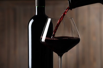 Photo of Pouring red wine into glass and bottles against blurred background, closeup